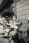 604413 Afbeelding van Peter van der Linden in het zitje achter op de fiets van zijn moeder, tegen de schutting naast de ...